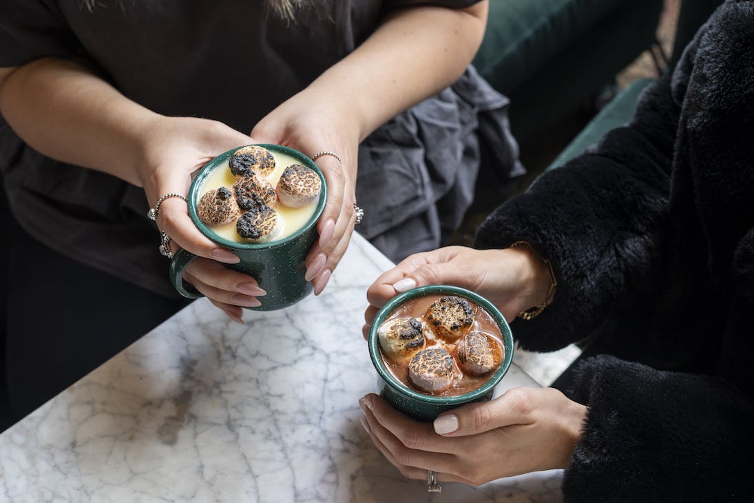 two people holding mugs of hot chocolate